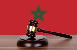 Auktionshammer / Richterhammer auf einem Holzuntergrund, vor der Flagge von Marokko