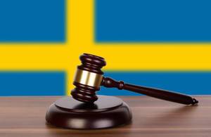 Auktionshammer / Richterhammer auf einem Holzuntergrund, vor der Flagge von Schweden