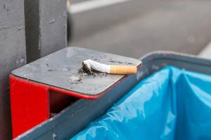 Ausgedrückte Zigarette der Marke Marlboro liegt auf metallener Halterung eines Mülleimers