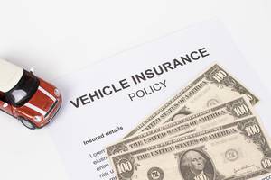 Autoversicherungsvertrag mit rotem Spielzeugauto und Dollar-Scheinen