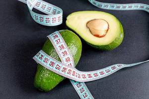Avocado and measuring tape on a black background. The concept of weight loss