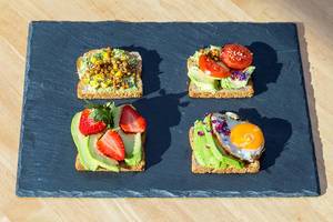 Avocado toasts with different toppings: lentils, strawberries, tomatoes and egg