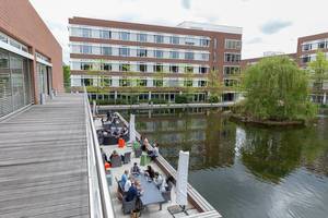 AXA-House in Cologne, Germany at Colonia-Allee with people relaxing on a terrace deck at a lake with a small island.