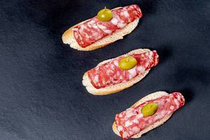 Baguette sandwiches with salami and olives on a black background. Top view (Flip 2019)