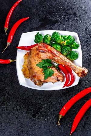 Baked chicken leg with Brussels sprouts and chili pepper on black background (Flip 2019)