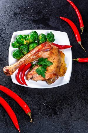 Baked chicken leg with Brussels sprouts and chili pepper on black background