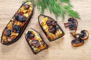 Baked eggplant with vegetables, couscous and mushrooms on a wooden background. Top view (Flip 2019)