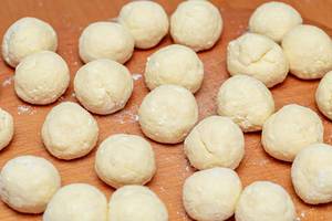 Balls with raw dough on a wooden table with flour