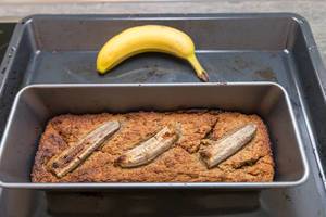 Banana pie in a baking tray surrounded by a ripe banana