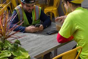 Bauarbeiter in Downtown Chicago sitzen in der Sonne und benutzen ihre Smartphones während einer Arbeitspause