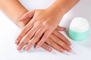 Beautiful woman hands with light manicure on nails and a jar of cream