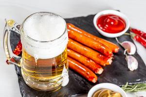 Beer mug with sauces and sausages on a black stone tray