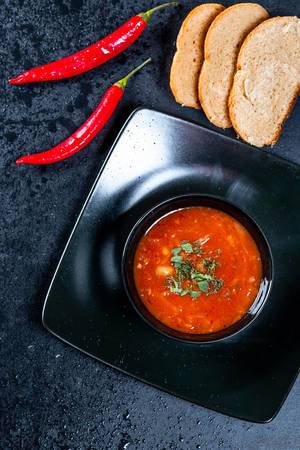 Beetroot tomato soup with slices of bread and chili on a black background