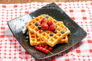 Belgian waffles with blueberries, strawberries and red currants on a black plate (Flip 2019)
