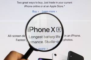 Beschreibungstext und Schriftzug des iPhone X vergrößert unter einem Lupenglas dargestellt