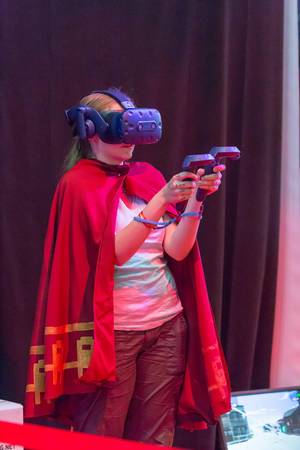 Besucherin mit Umhang zockt mit VR Headset und Controllern