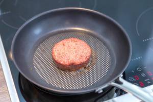 Beyond Meat Patty - das vegane Burger-Pastetchen - wird in einer schwarzen Bratpfanne auf einer Induktionsherd gebraten