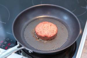 Beyond Meat Patty - the vegan alternative of burger meat - is being fried in a frying pan on an induction stove