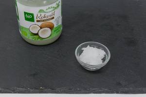 Bio-Kokosöl im Glas mit Muster in Schale auf schwarzer Platte