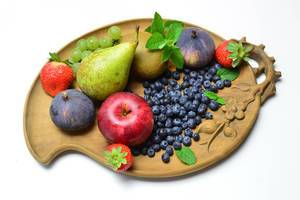 Birne mit Apfel, Kiwi, Feigen, Erdbeeren, Blaubeeren und Weintrauben auf Obstschale