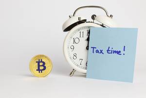 Bitcoin-Kryptocurrency, vintage alarm clock and tax time written on a post-it