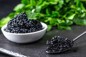 Black caviar on a dark stone background with greens