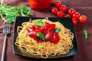 Black plate with delicious spaghetti with vegetables and fork