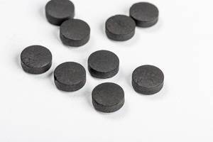 Black tablets of activated carbon on a white background