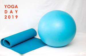 Blaue Yogamatte und Gymnastikball vor weißem Hintergrund, mit dem Bildtitel "Yoga Day 2019" - Tag des Yoga