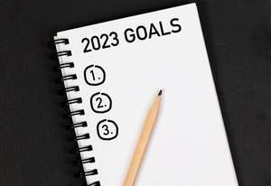 Bleistift und Notizheft mit Zielen für 2023 auf einem schwarzen Tisch