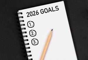 Bleistift und Notizheft mit Zielen für 2026 auf einem schwarzen Tisch