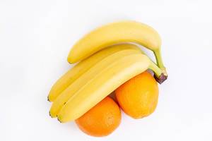 Blick auf reife Bananen und zwei Orangen, auf einer weißen Oberfläche