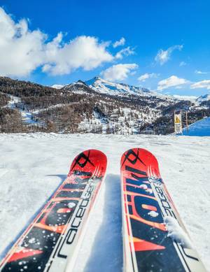 Blick über orangenes Paar Ski auf Skipiste und Berge in Wintersportgebiet Vars, Frankreich