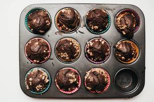 Blick von oben auf frisch gebackene Schokoladen-Muffins mit Nüssen in farbigen Kuchenförmchen aus Papier in schwarzer Muffin-Backform