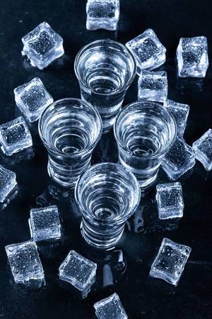 Blick von oben auf vier Gläser mit kaltem Wodka umringt von Eiswürfeln auf schwarzem Hintergrund