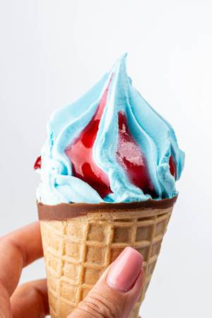 Blue ice cream with jam in waffle cone in hand