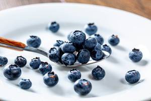 Blueberries in a spoon and scattered on a white plate