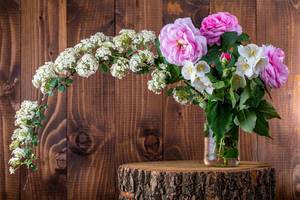 Blumenstrauß mit verschiednen Rosa und weißen Blumen, in einer Glasvase auf einem dekorativen Baumstamm