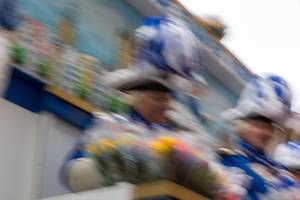Blurred snapshot of Carnival in Cologne with two men in traditional blue-white costumes throwing roses during the Rose Monday parade