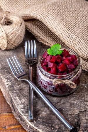 Boiled beet cubes in a glass jar on a wooden background with burlap and forks