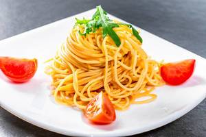 Boiled spaghetti with tomato slices and arugula leaves