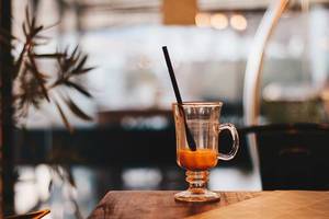 Bokeh Photo of Glass Cup of Coffee on Wooden Table with Cafe in the Background