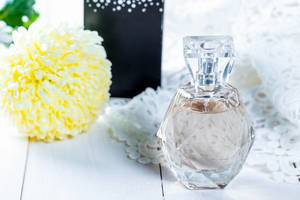 Bottle of perfume with flower on white wooden background