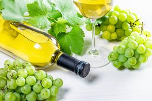 Bottle of white wine, glass, green grapes and leaves on white table (Flip 2019)