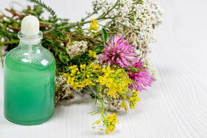 Bottle with green cosmetic and a bouquet of wild flowers on a white wooden background. The concept of natural cosmetics