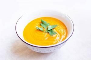 Bowl of carrot cream soup with parsley on top on white background