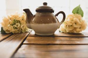Braune Teekanne aus Keramik mit weißen Blumensträußen auf einem Holztisch