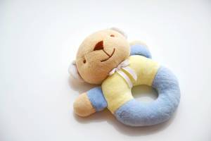 Brauner Teddybär mit weißer Schleife um den Hals und blau-gelbem Körper in Form eines Beißrings vor weißem Hintergrund