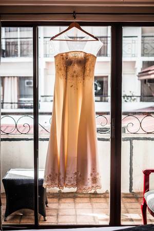 Brautkleid hängt an Fenster vor Balkon im Altbau-Stil – Lichteinfall durch Scheibe schimmert durch Kleid
