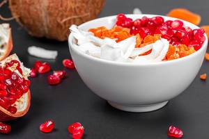 Breakfast background with oatmeal, coconut, pomegranate seeds and dried apricots in a white bowl